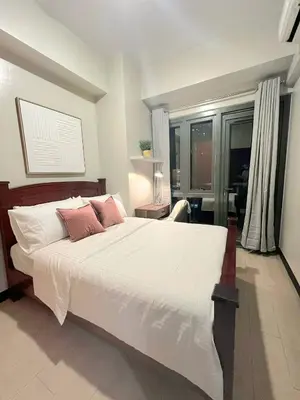 a bedroom with a large white bed with pink pillows at Greenbelt Hamilton Residences by ChiKat in Manila