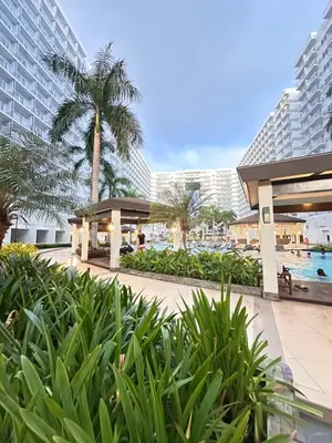 a resort with a pool and palm trees and buildings at Shell Residences MOA Paul's Place in Manila