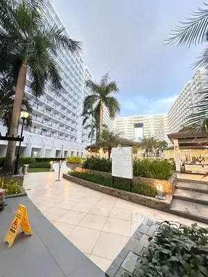 a walkway in front of a large building with palm trees at Shell Residences MOA Paul's Place in Manila