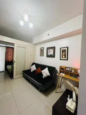a living room with a black couch and a table at Allie's Cozy Place at Sea Residences in Manila