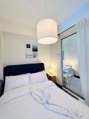 a bedroom with a white bed with a large window at Prisma Residences by Kozy Mood near BGC in Manila