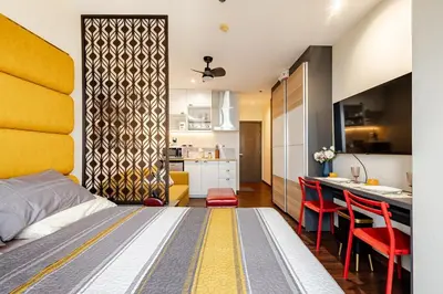 a bedroom with a bed and a kitchen with red chairs at Opulent Condo Knightsbridge Residences in Manila