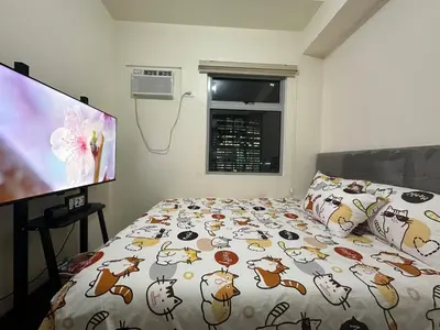 a bedroom with a bed with a comforter and a tv at Staycation in Sucat Road in Manila