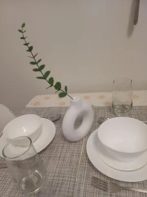 a table with white plates and a vase and glasses at Cozy Pad-50th in Manila