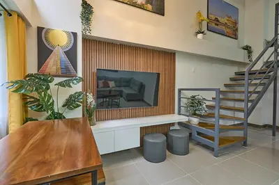 a living room with a television and a staircase at Modern Loft-Style Condo - Perfect for Families or Couples in Manila