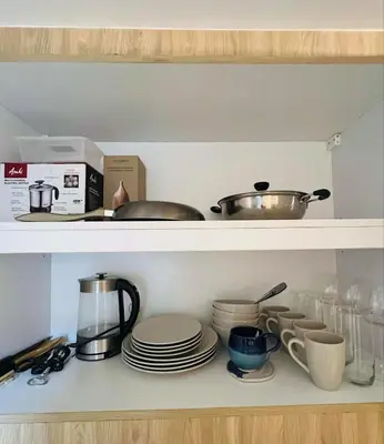 a kitchen shelf with dishes and pots and pans at Sarah's Place at Light Residences in Manila