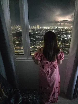 a little girl looking out of a window at night at 2 BR Penthouse with Sunset View in Manila