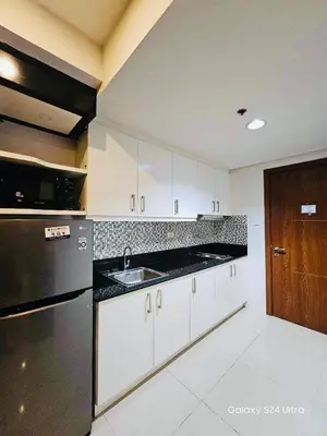 a kitchen with white cabinets and a black refrigerator at Quaint 2BR Connected Apartment in Pasay City - Perfect for Families front of MOA in Manila