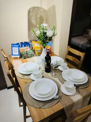 a wooden table with white plates and a vase with flowers at 1-Bedroom Condo - Stunning Sunset at the City in Manila