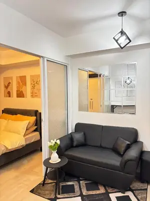 a living room with a black couch and a bed at Staycation in Oasis in Manila