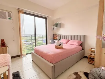 a bedroom with a bed with pink pillows and a window at Nuvali Sta Rosa Laguna in Pulong Cacawate