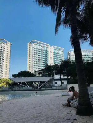 a man sitting on the beach next to a palm tree at Azure Urban Condomiun Near Airport in Manila