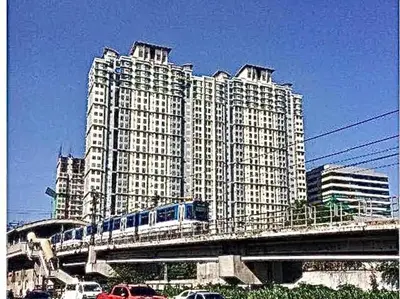 a train on a bridge in front of a large building at 1 Br - Royalty Vacation - Edsa Makati in Manila