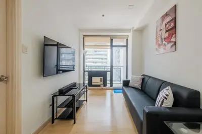 a living room with a black couch and a television at Free Parking at Gramercy with Big TV and Fast WiFi in Manila