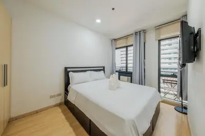 a bedroom with a large white bed and a television at Free Parking at Gramercy with Big TV and Fast WiFi in Manila