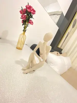 a wooden doll sitting on a bed next to a vase of flowers at The Courtyard Contemporary Studio at Taguig WiFi in Manila