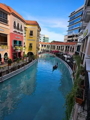 a boat in a canal in a city with buildings at Elivion Staycations in McKinley Hill BGC with Pool near Venice Mall in Manila