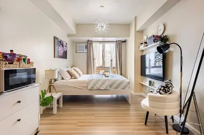 a bedroom with a bed and a television and a chair at Studio Lune - Heart of Makati in Manila