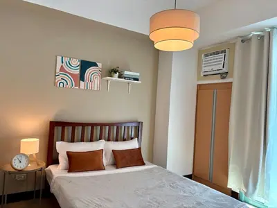 a bedroom with a bed and a clock and a window at Warm & Minimalist 1BR at Two Palm, Newport, T3 in Manila