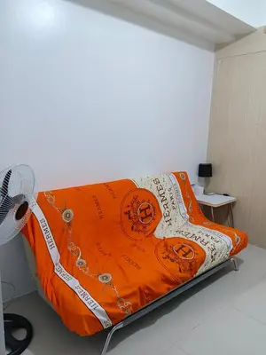 a bed with an orange blanket and a fan at Rosaland staycation in Manila