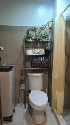 a bathroom with a toilet and a shelf with plants at Urban Haven Manila in Manila