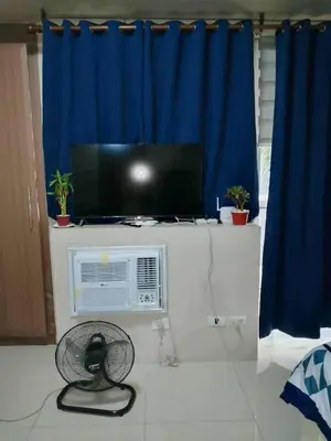 a room with a tv and a fan and a blue curtain at Neri Ann's Comfort Escape in Manila