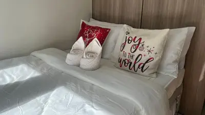 a bed with white slippers and a pillow with joy to the world at Kabina Suites at Fame Residences in Manila