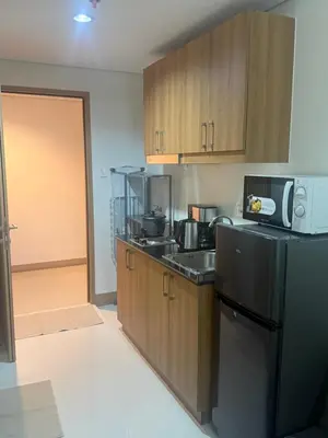 a kitchen with wooden cabinets and a black refrigerator at The Vibe at SMDC The Lush Residences in Manila