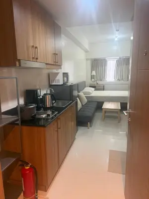 a kitchen with wooden cabinets and a living room at The Vibe at SMDC The Lush Residences in Manila