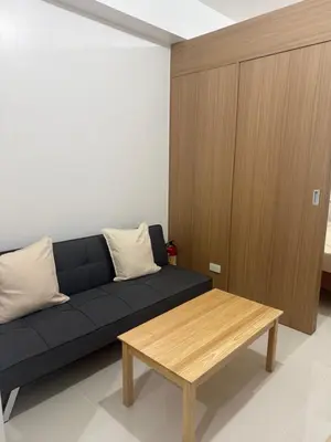 a living room with a black couch and a wooden table at The Fortress at SMDC The Lush Residences in Manila