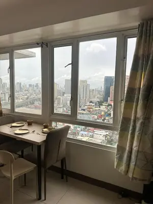 a table and chairs in a room with a large window at Next Abode Modern Stay at TheBeaconMakatiRoces in Manila