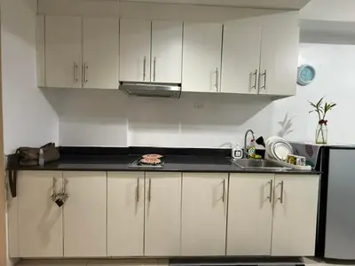 a kitchen with white cabinets and a black counter top at Staycation at Sea Residences MOA Pasay City in Manila