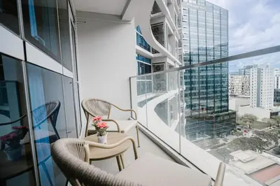a balcony with chairs and a table with a view of a city at CozyBGCCondoKing BedFast WiFiSteps fromUptownMall in Manila