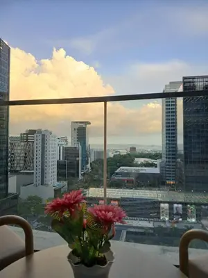 a vase with flowers on a table in front of a window at CozyBGCCondoKing BedFast WiFiSteps fromUptownMall in Manila