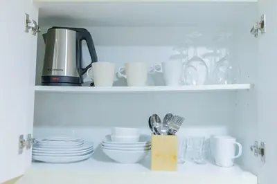 a shelf with cups and plates and a coffee maker at CozyBGCCondoKing BedFast WiFiSteps fromUptownMall in Manila