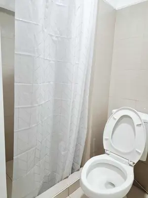 a bathroom with a toilet with a white shower curtain at Oasis at Shore Residences in Manila