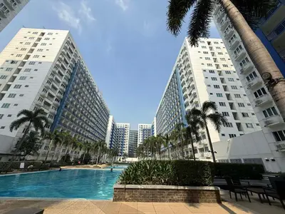 two tall buildings with a swimming pool and palm trees at Sea Residences - Mall of Asia 829B by Forever-mc Condotel in Manila