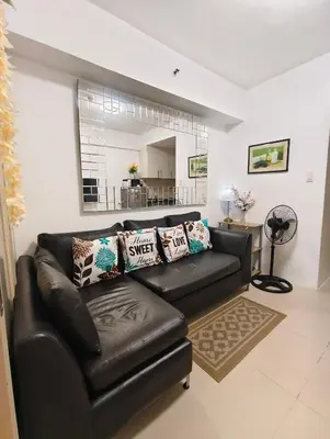 a living room with a black leather couch and a mirror at Juliza's MOA Staycation in Manila