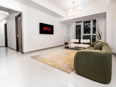 a living room with a couch and a tv on a wall at Modern 2-Bedroom BGC Condo by Uptown Mall in Manila