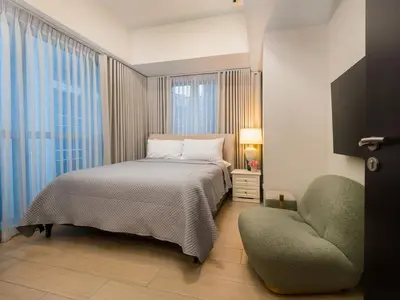 a bedroom with a bed and a chair next to a window at Modern 2-Bedroom BGC Condo by Uptown Mall in Manila