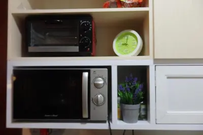a microwave in a cabinet with a clock and flowers at The Cube at 15th in Taytay