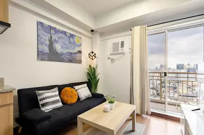 a living room with a black couch and a window at Stylish Condo - Cozy Urban Living in Manila