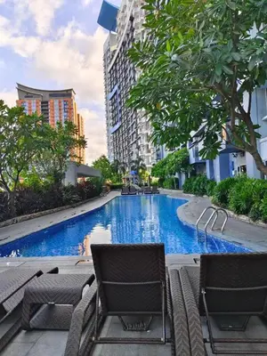 a large swimming pool with chairs and trees and buildings at Cozy Manhattan Heights 1 Bedroom Araneta Cubao in Manila