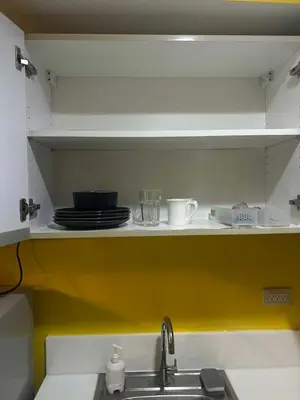 a kitchen shelf with plates and cups and a sink at Sunbeam - Air Residence 42nd floor in Manila