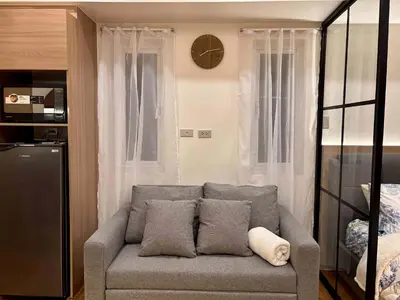 a living room with a gray couch and a clock at GRACE RESIDENCES Condo in Manila