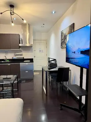 a living room with a kitchen and a large screen tv at The Gramercy Residences in Manila