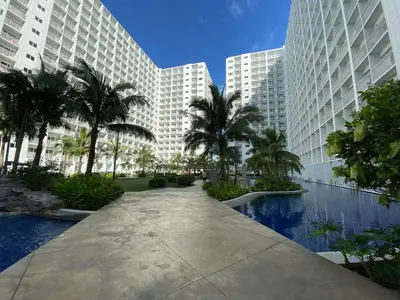 a large building with palm trees and a swimming pool at Cozy 1 BR unit at Shore 1 Residences Mall of Asia in Manila
