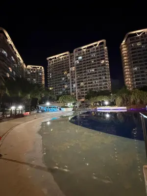 an empty swimming pool at night with tall buildings at Azure SYM Staycation in Manila