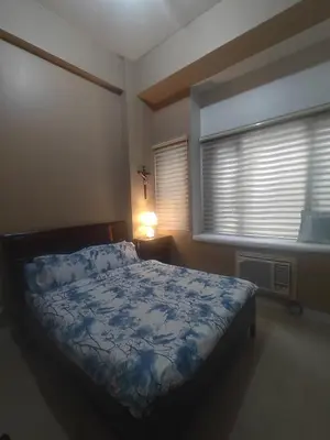 a bedroom with a bed with a blue comforter and a window at Cozy Condo Across NAIA T3 One Palm Tree in Manila