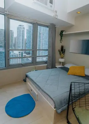 a bedroom with a large bed with blue sheets and large windows at Chic Eastwood City Studio w Pool and Gym Access in Manila
